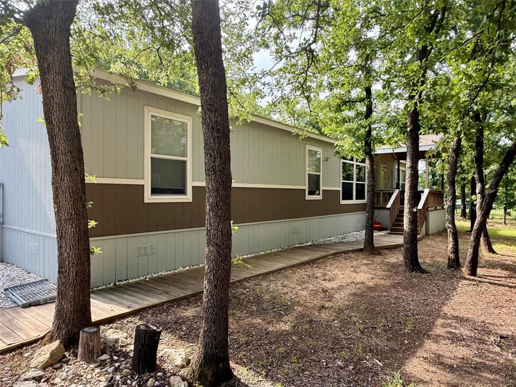 145 Adalida Lane Springtown, TX 76082 - Photo 2 of 29 Exterior siding featuring a multi-tone panel design, white-framed windows, a wooden walkway, and mature trees