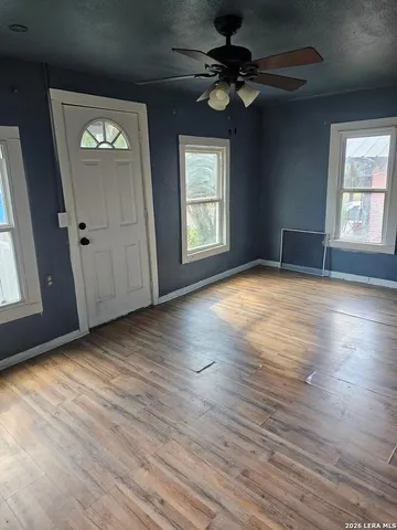 an empty room with wooden floor chandelier fan and windows