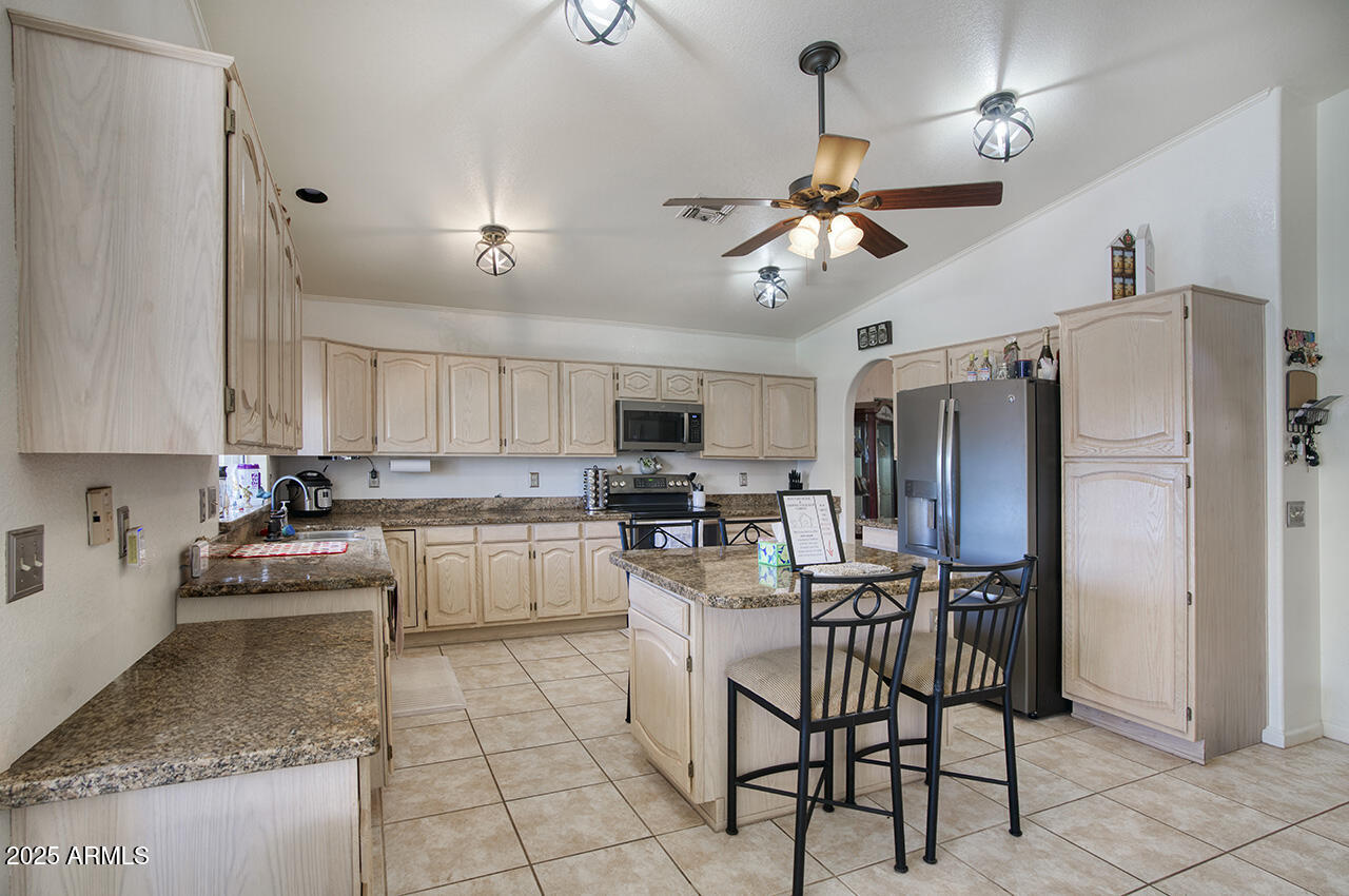 12677 North 77th Drive Peoria, AZ 85381 - Photo 6 of 25 a kitchen with stainless steel appliances kitchen island granite countertop a refrigerator a stove a sink a dining table and chairs with wooden floor