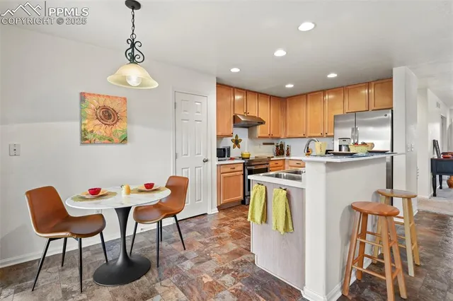 a kitchen with stainless steel appliances granite countertop a dining table chairs refrigerator and sink
