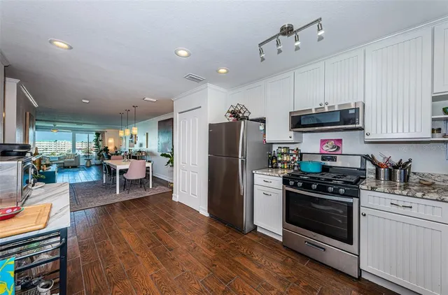 a white kitchen with stainless steel appliances granite countertop a refrigerator stove a sink dishwasher and white cabinets with wooden floor