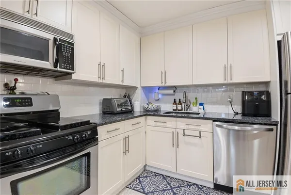 a white kitchen with stainless steel appliances granite countertop a stove a sink and white cabinets