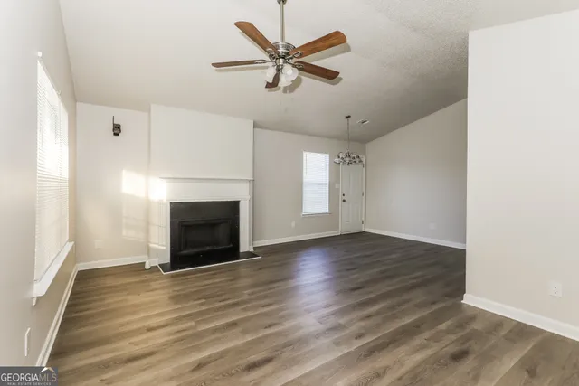 an empty room with wooden floor a ceiling fan a fireplace and windows