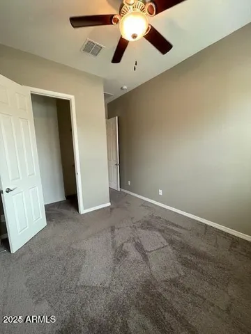 an empty room with chandelier fan and kitchen view