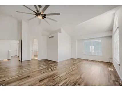 a view of an empty room with wooden floor and a ceiling fan