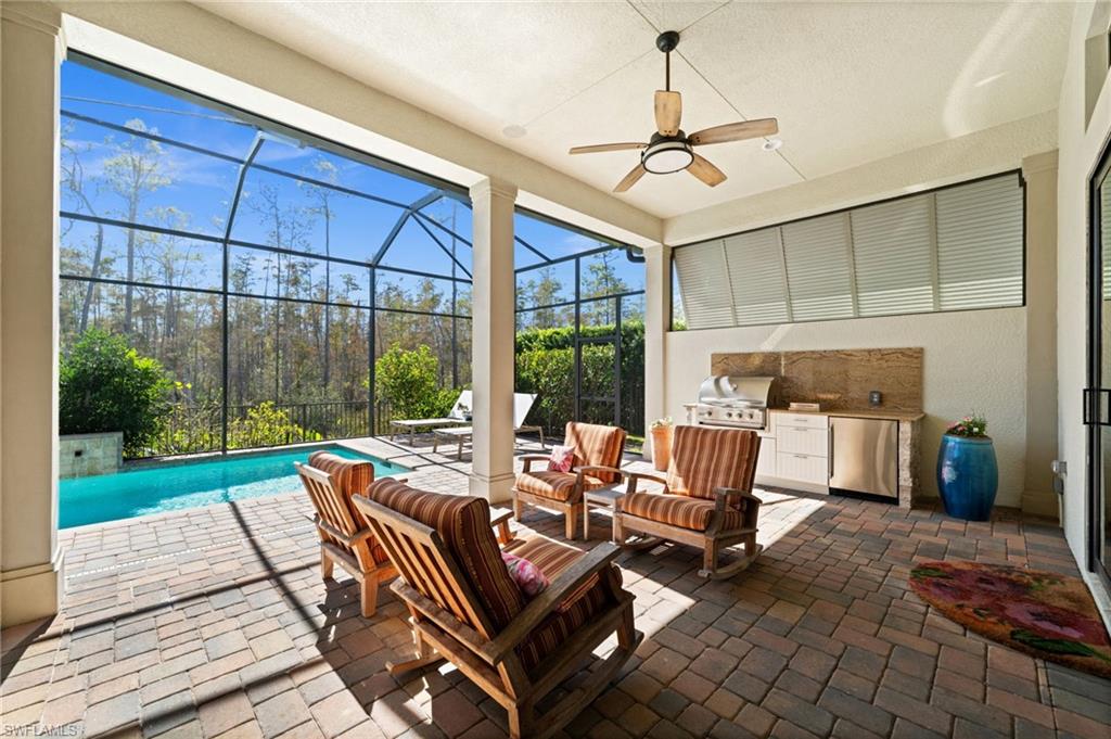 14686 Reserve Place Naples, FL 34109 - Photo 32 of 48 Covered patio with an outdoor kitchen setup and seating, which opens to the pool deck through large sliding glass doors.