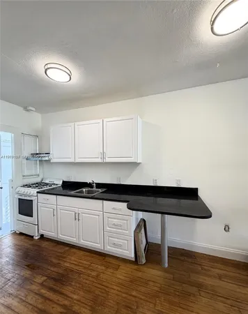 a kitchen with granite countertop a stove a sink and white cabinets