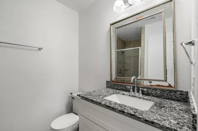 a bathroom with a granite countertop sink toilet and mirror