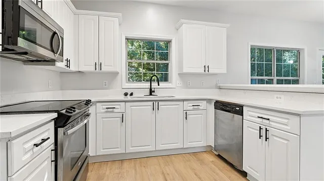 a kitchen with white cabinets stainless steel appliances a sink and a window