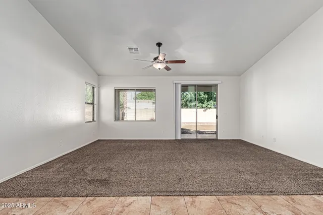 an empty room with chandelier fan and windows