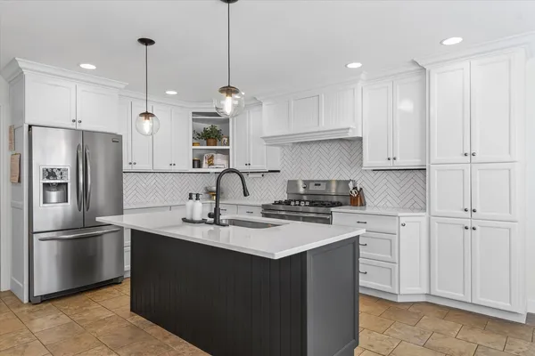 a kitchen with stainless steel appliances granite countertop a sink a stove a refrigerator and white cabinets