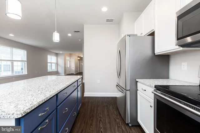 a kitchen with stainless steel appliances granite countertop a refrigerator a sink dishwasher a stove and white countertops with wooden floor