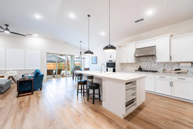 a kitchen with stainless steel appliances kitchen island granite countertop a dining table chairs and white cabinets