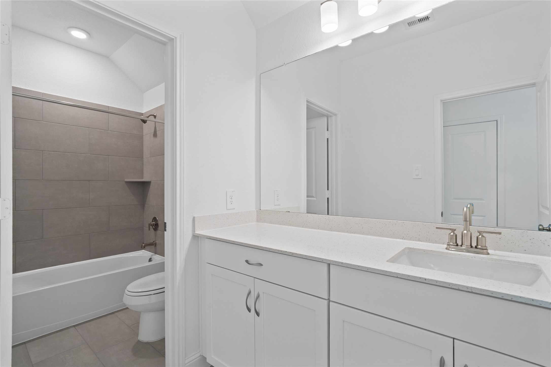 17315 July Moon Lane Conroe, TX 77302 - Photo 36 of 46 Secondary bathroom featuring an extended vanity cabinet with single bowl sink, brushed nickel hardware, mirror and vanity lighting, tub/shower combination with tile surround and tile flooring.