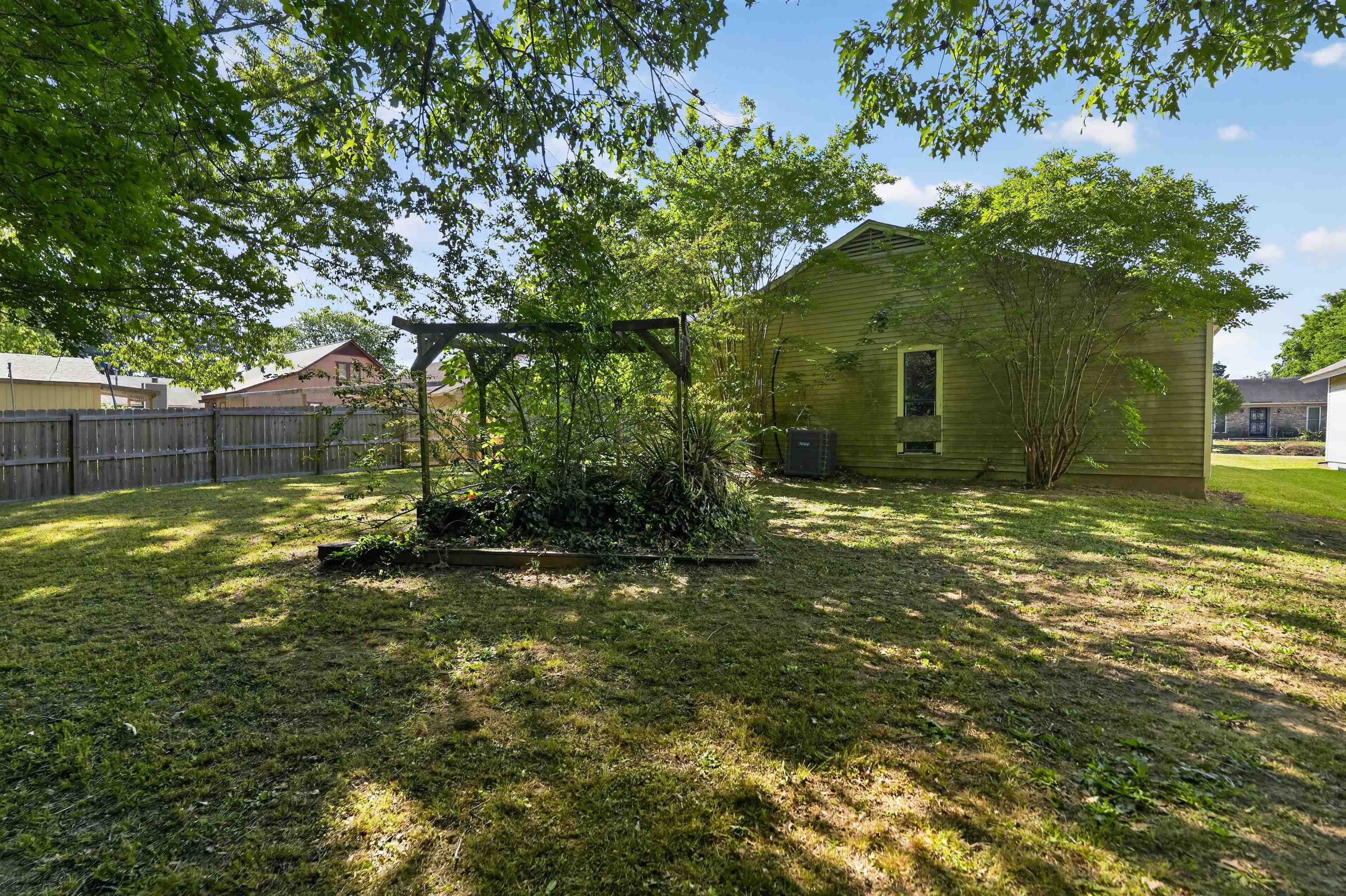 3372 Spring Shadow Drive Memphis, TN 38118 - Photo 5 of 35 Expansive backyard featuring a wood privacy fence, mature trees, a wooden pergola, and a side exterior wall with a window