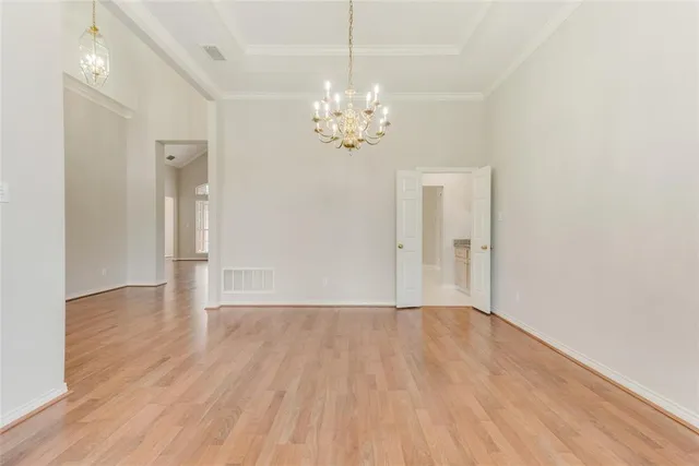 a view of an empty room with chandelier and wooden floor