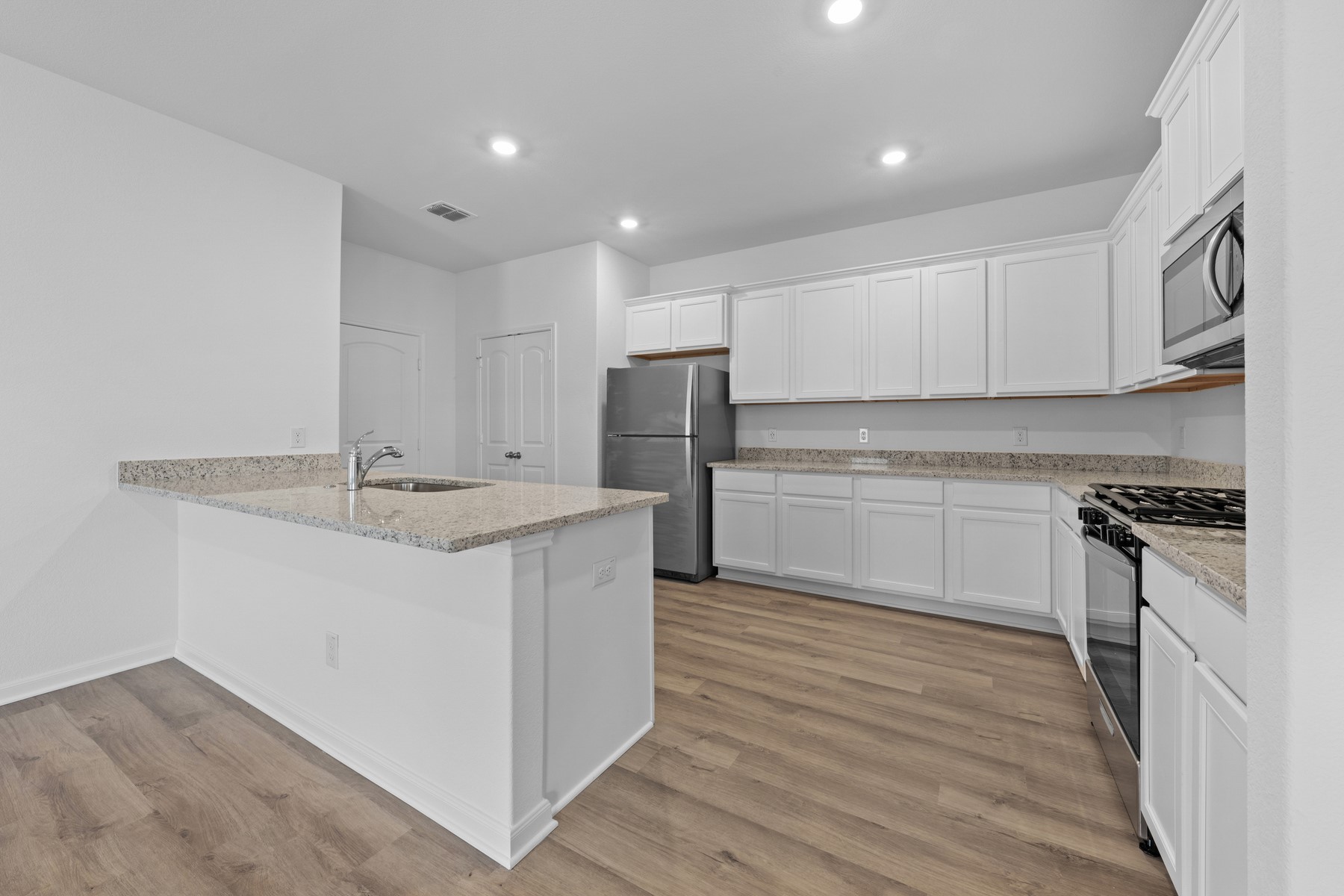 197 Fairlawn Way Maxwell, TX 78656 - Photo 4 of 14 Kitchen featuring appliances with stainless steel finishes, light stone counters, white cabinetry, light wood-style flooring, and recessed lighting