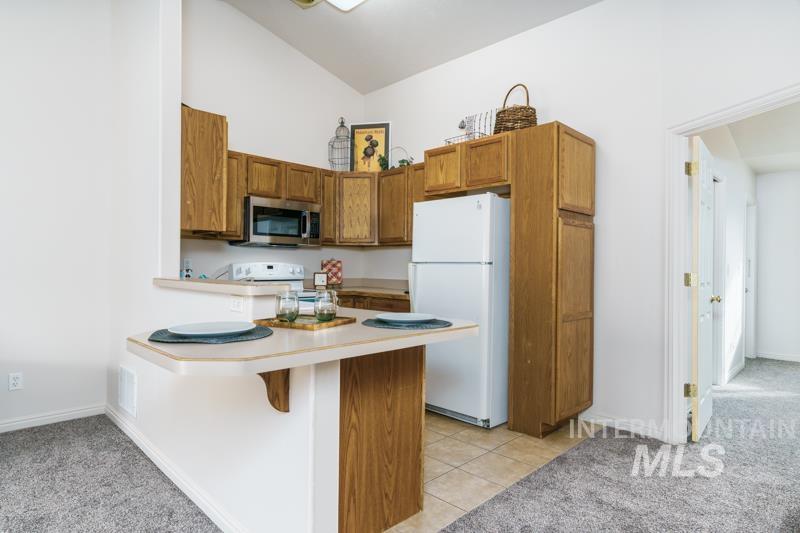 204 La Valle Strada Pocatello, ID 83201 - Photo 7 of 23 Kitchen featuring light colored carpet, brown cabinets, white appliances, light countertops, and high vaulted ceiling