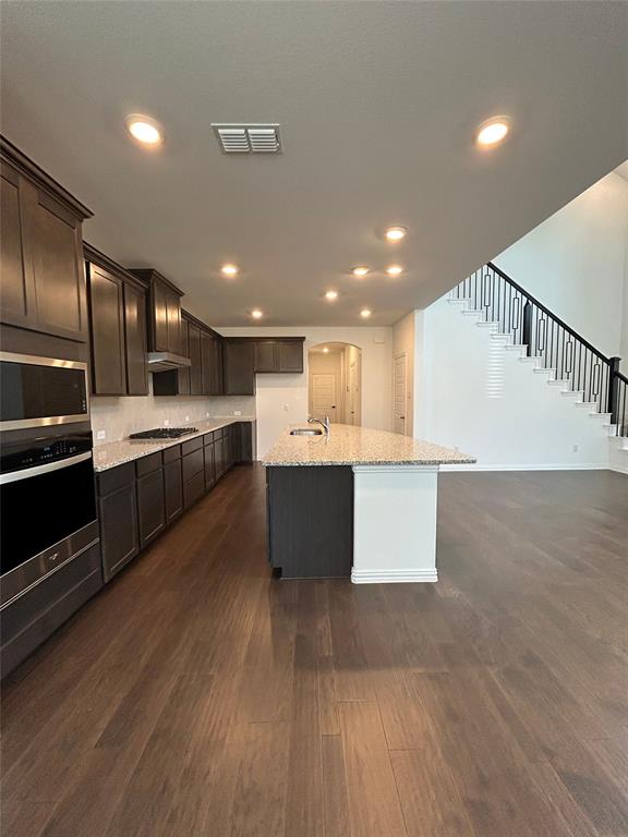 1448 Sun Gdn Way Justin, TX 76247 - Photo 2 of 28 Kitchen featuring light stone counters, arched walkways, dark wood-style floors, stainless steel appliances, and an island with sink