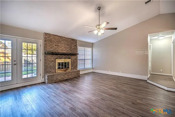 an empty room with wooden floor fireplace and windows