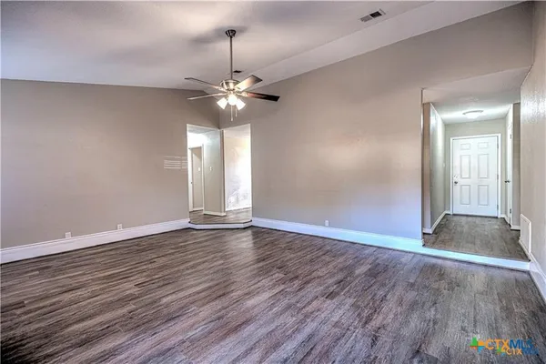 a view of an empty room with wooden floor and a ceiling fan