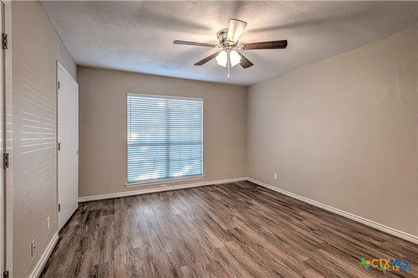 an empty room with wooden floor chandelier fan and windows