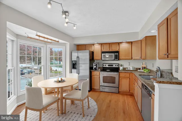 a kitchen with stainless steel appliances granite countertop a stove top oven a sink dishwasher a dining table and chairs with wooden floor