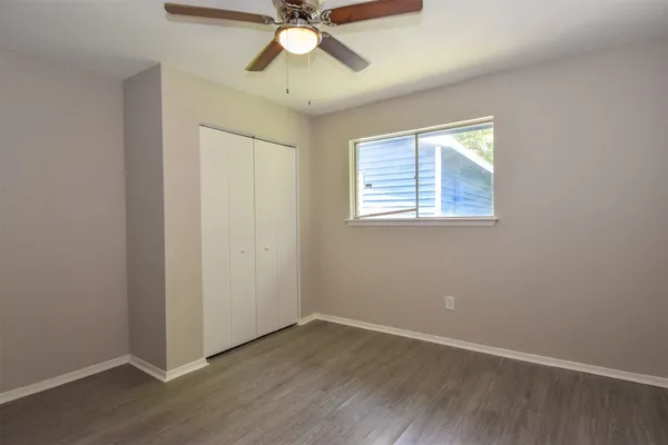 an empty room with wooden floor fan and windows