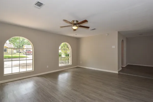 an empty room with wooden floor chandelier fan and windows