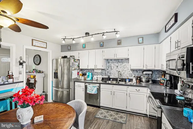 a kitchen with stainless steel appliances kitchen island granite countertop a refrigerator a sink dishwasher and white cabinets with wooden floor