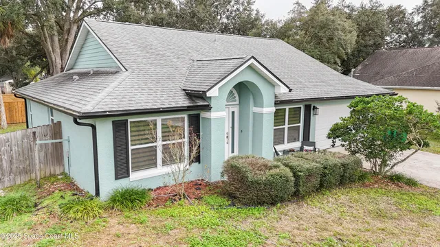 a view of a white house with a small yard and large trees