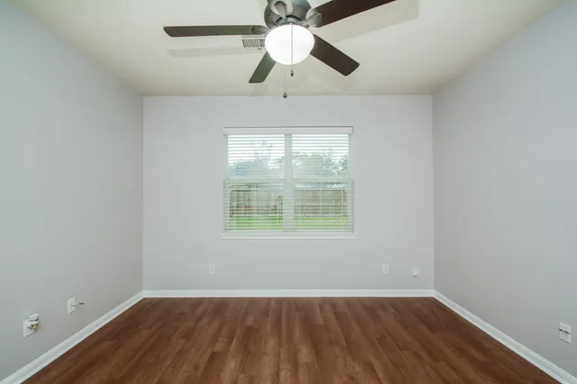 an empty room with wooden floor chandelier fan and windows