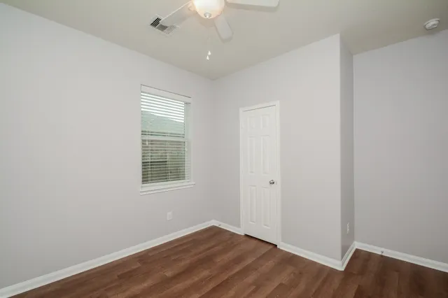 an empty room with wooden floor chandelier fan and windows