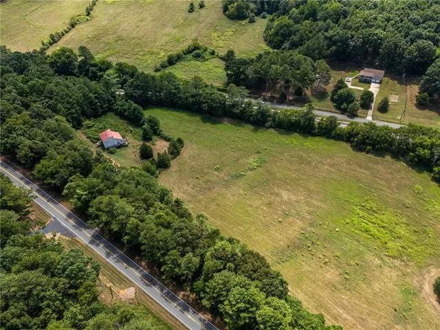 an aerial view of a residential houses with outdoor space and trees all around