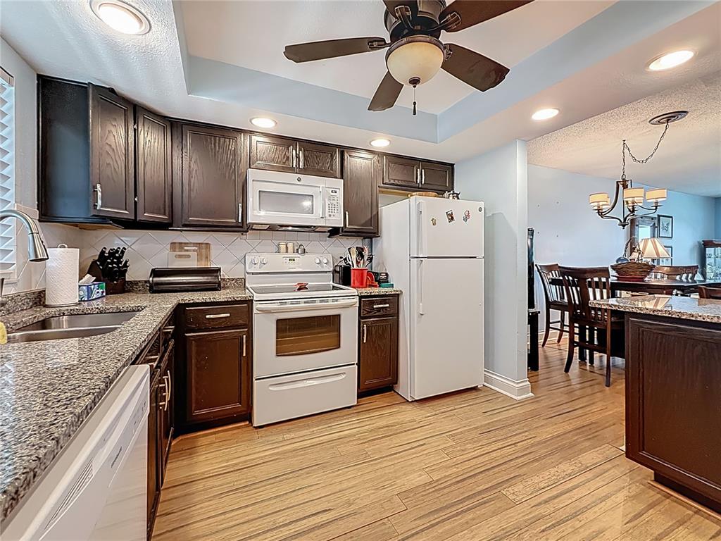 4725 Cove Circle, Unit 908 St. Petersburg, FL 33708 - Photo 14 of 61 a kitchen with kitchen island granite countertop a refrigerator a stove top oven a sink dishwasher and white cabinets with wooden floor