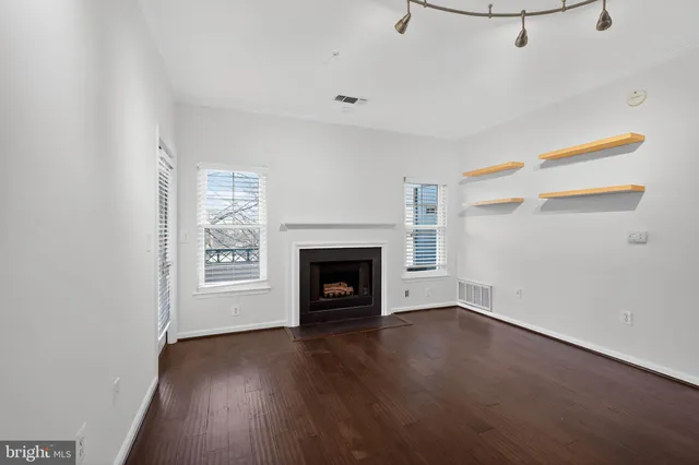 a view of an empty room with wooden floor fireplace and a window