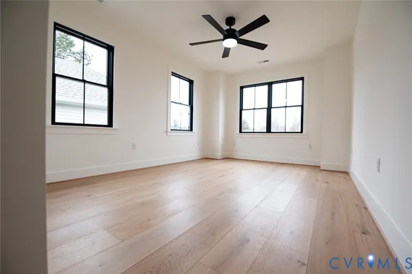 an empty room with wooden floor windows and ceiling fan