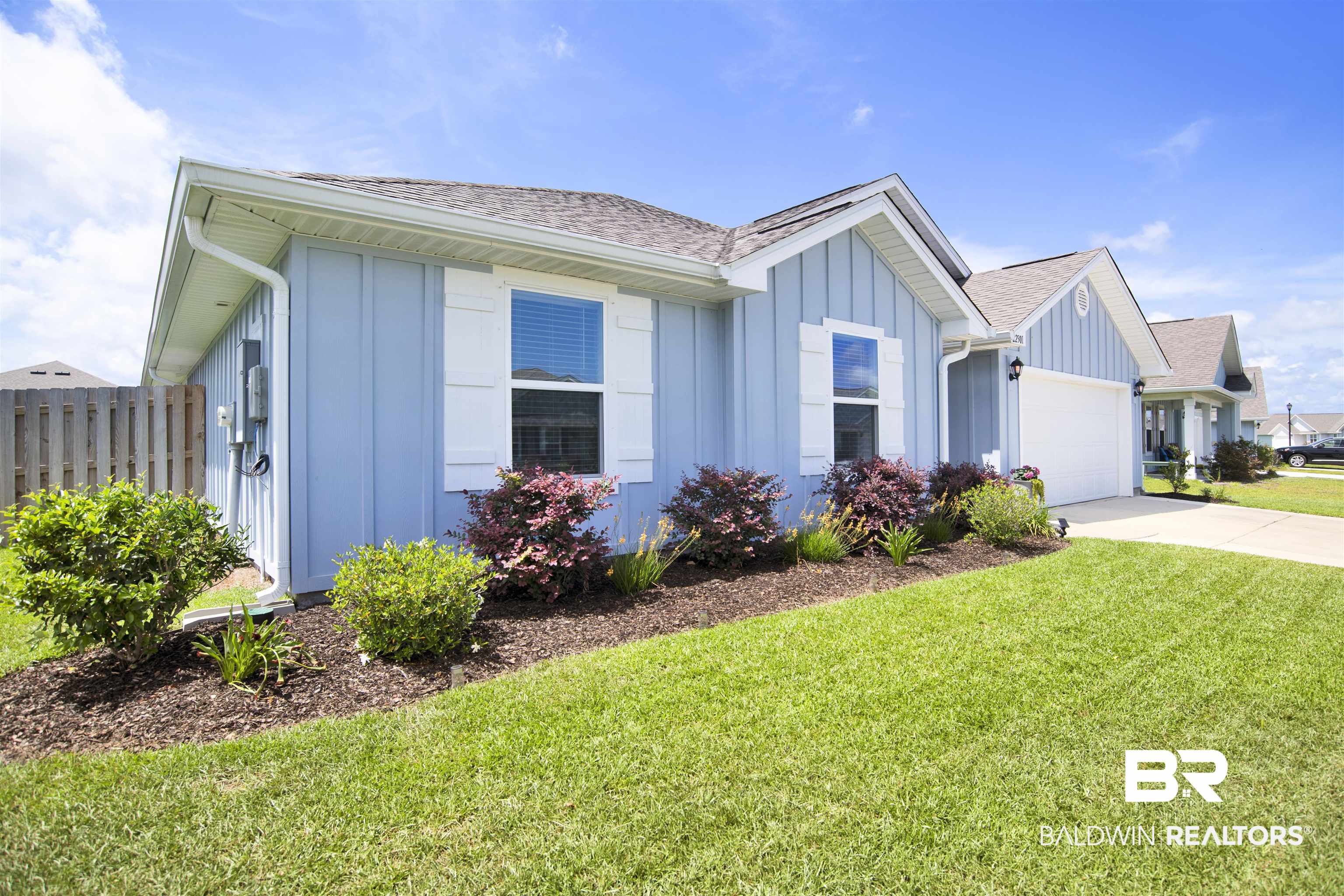 22301 Early Dawn Circle Foley, AL 36535 - Photo 3 of 45 Residential exterior featuring light blue vertical siding, white window shutters, a front-facing garage, a concrete driveway, and a landscaped front yard with green lawn