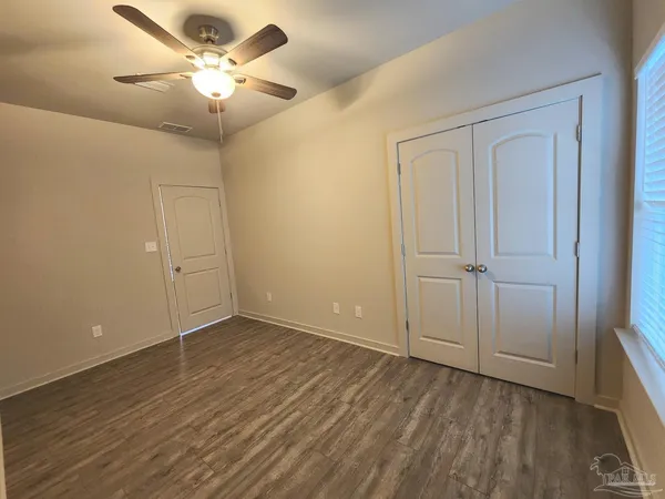 an empty room with wooden floor fan and windows
