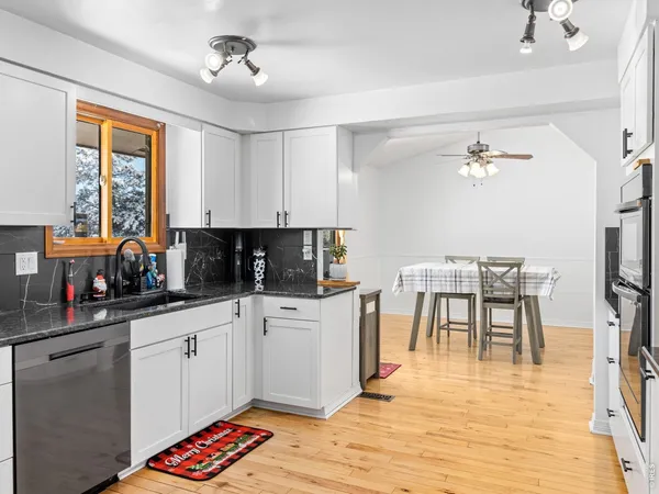 a kitchen with stainless steel appliances granite countertop a stove top oven a sink a dining table and chairs with wooden floor