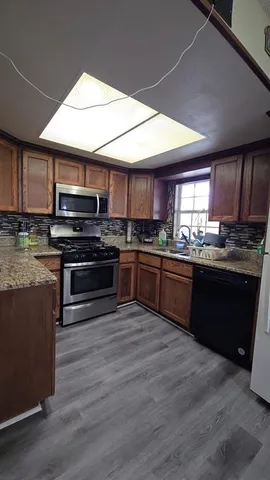 a kitchen with stainless steel appliances kitchen island granite countertop a stove a sink dishwasher and a microwave oven with wooden floor