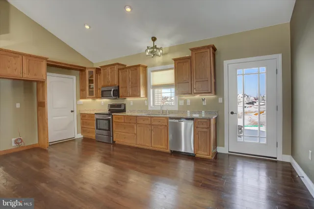 a kitchen with granite countertop a refrigerator oven a sink dishwasher and white cabinets with wooden floor