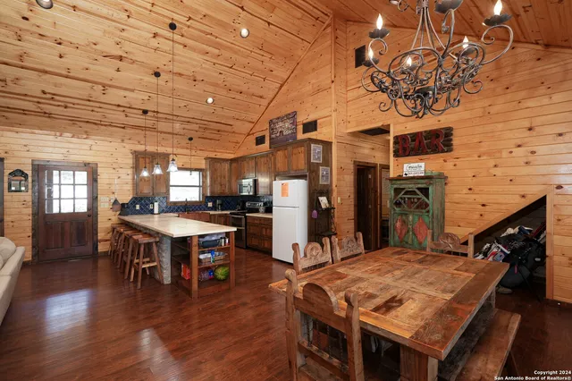 a dining hall with stainless steel appliances granite countertop a stove a refrigerator a kitchen island a dining table and chairs with wooden floor