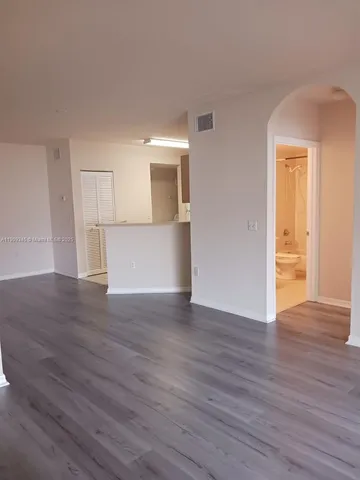 a view of empty room with wooden floor and kitchen