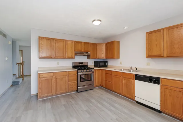 a kitchen with stainless steel appliances granite countertop a stove top oven a sink dishwasher and a refrigerator with wooden floor