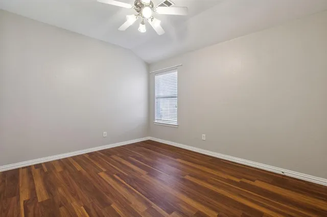 a view of an empty room with wooden floor and a chandelier fan