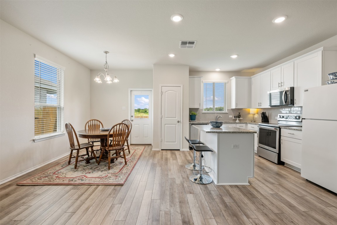 225 Gunther Way Taylor, TX 76574 - Photo 12 of 40 a kitchen with stainless steel appliances granite countertop a refrigerator a stove top oven a sink dishwasher a dining table and chairs with wooden floor