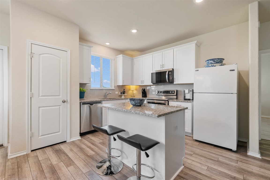 225 Gunther Way Taylor, TX 76574 - Photo 16 of 40 a kitchen with stainless steel appliances granite countertop a refrigerator stove a sink and white cabinets with wooden floor