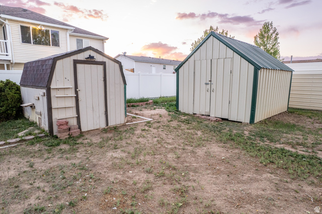 634 South 2100th Street West Vernal, UT 84078 - Photo 61 of 71 Expansive backyard area featuring two detached storage sheds, a privacy fence, and partial views of the main residence with a balcony