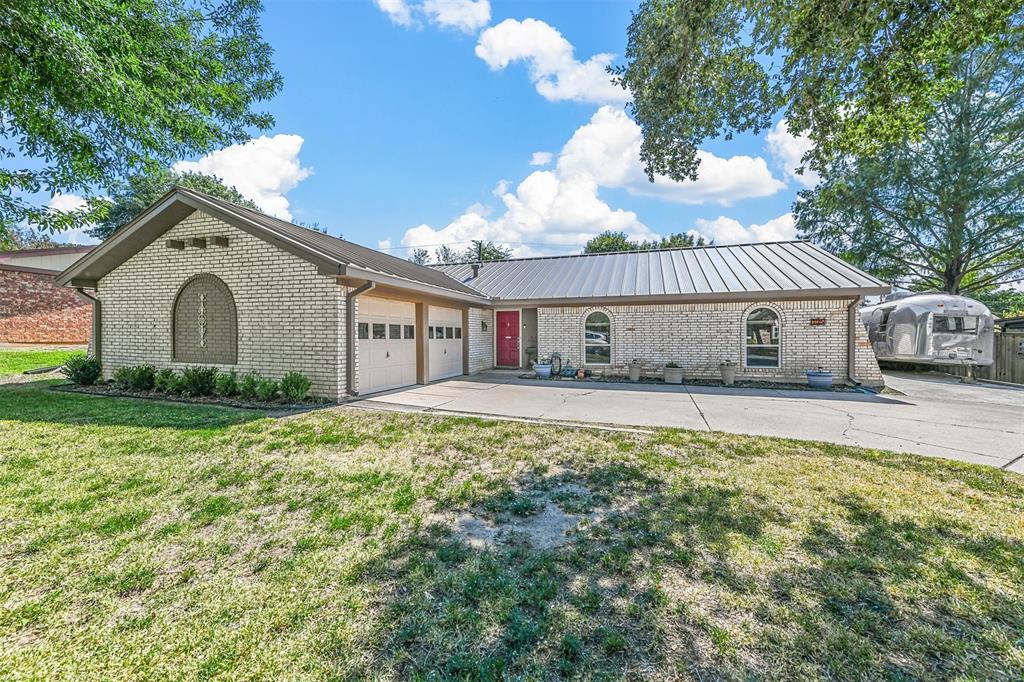 Ranch-style home with brick siding, concrete driveway, metal roof, a garage, and a front lawn